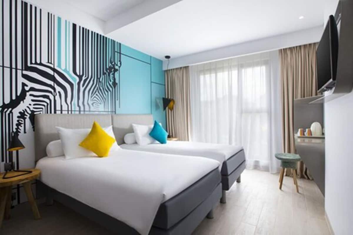 Ein modernes Hotelzimmer mit zwei Betten, einem großen Wandbild, einem Flachbildfernseher und einer kleinen Sitzecke.