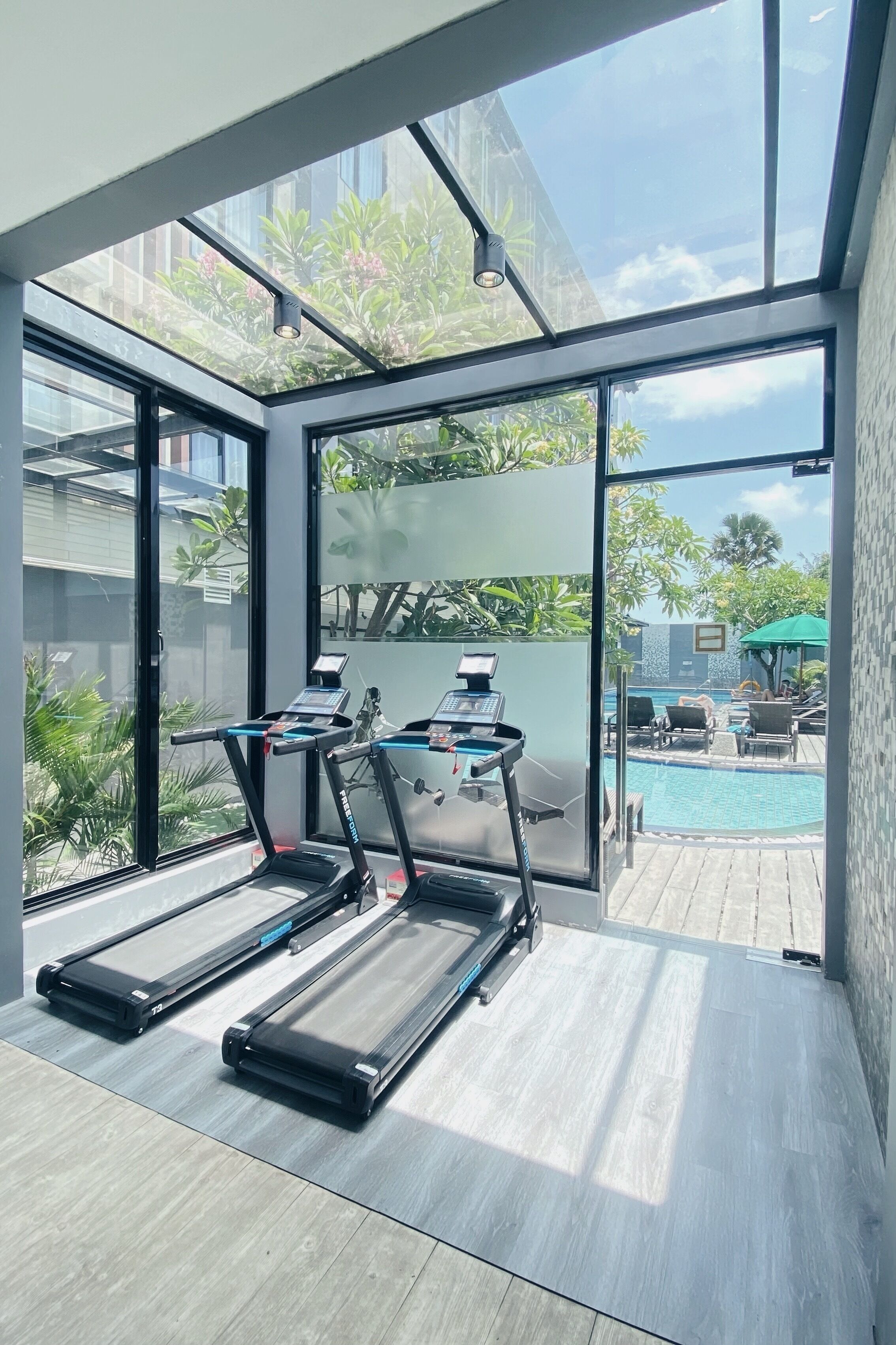 A modern gym with treadmills and a view of a swimming pool and outdoor seating.
