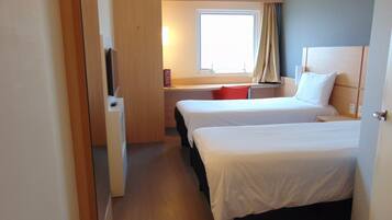 A hotel room with two beds, a desk, a TV, and a window with curtains.