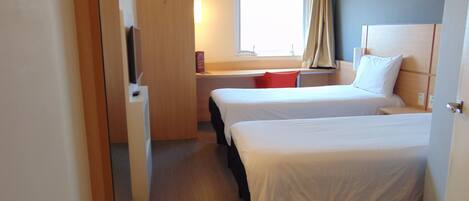 A hotel room with two beds, a desk, a TV, and a window with curtains.