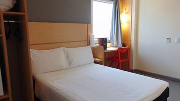 Una habitación de hotel con cama, escritorio, silla y armario.