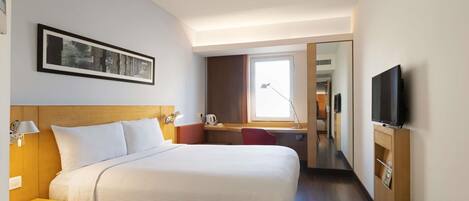 Habitación de hotel con una cama grande, mesitas de noche, un escritorio, una silla, un televisor y una ventana.