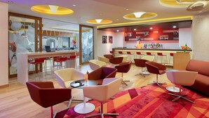 A modern bar area with a bar counter, red chairs, and a patterned carpet.
