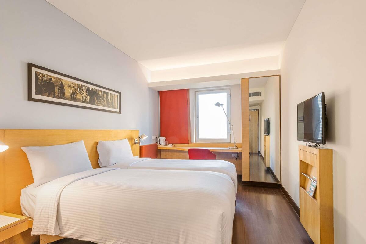 Une chambre d’hôtel avec deux lits, un bureau, une télévision et un tableau au mur.