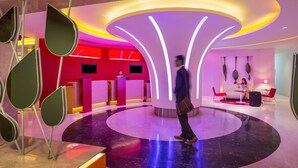 A modern lobby with a central circular seating area, a reception desk, and a seating area with a sofa and chairs.
