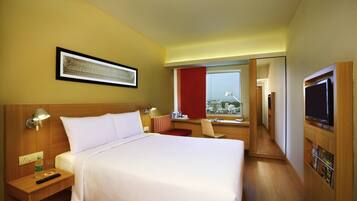 A hotel room with a bed, bedside table, lamp, TV, and a window with a city view.