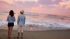 Two people standing on a beach, facing the ocean during sunset.