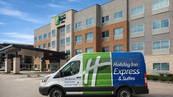 Una camioneta Holiday Inn Express & Suites estacionada frente a un hotel de diseño moderno, con varios pisos y una entrada cubierta.