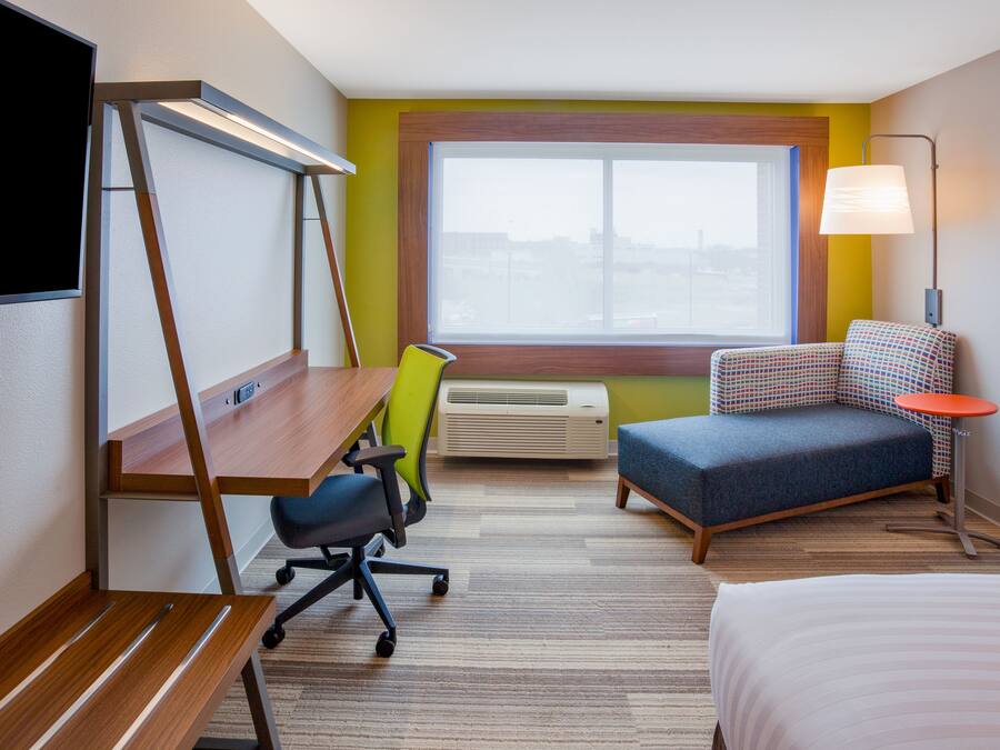 Una habitación de hotel con escritorio, silla, sofá, cama y un ventanal grande.