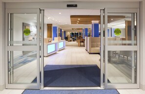 A hotel lobby with a reception desk, seating area, and a blue carpet leading to the entrance. - Holiday Inn Express & Suites Des Moines Downtown by IHG (Des Moines)