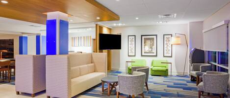 A hotel lobby with a sofa, chairs, a TV, artwork on the wall, and a patterned carpet.