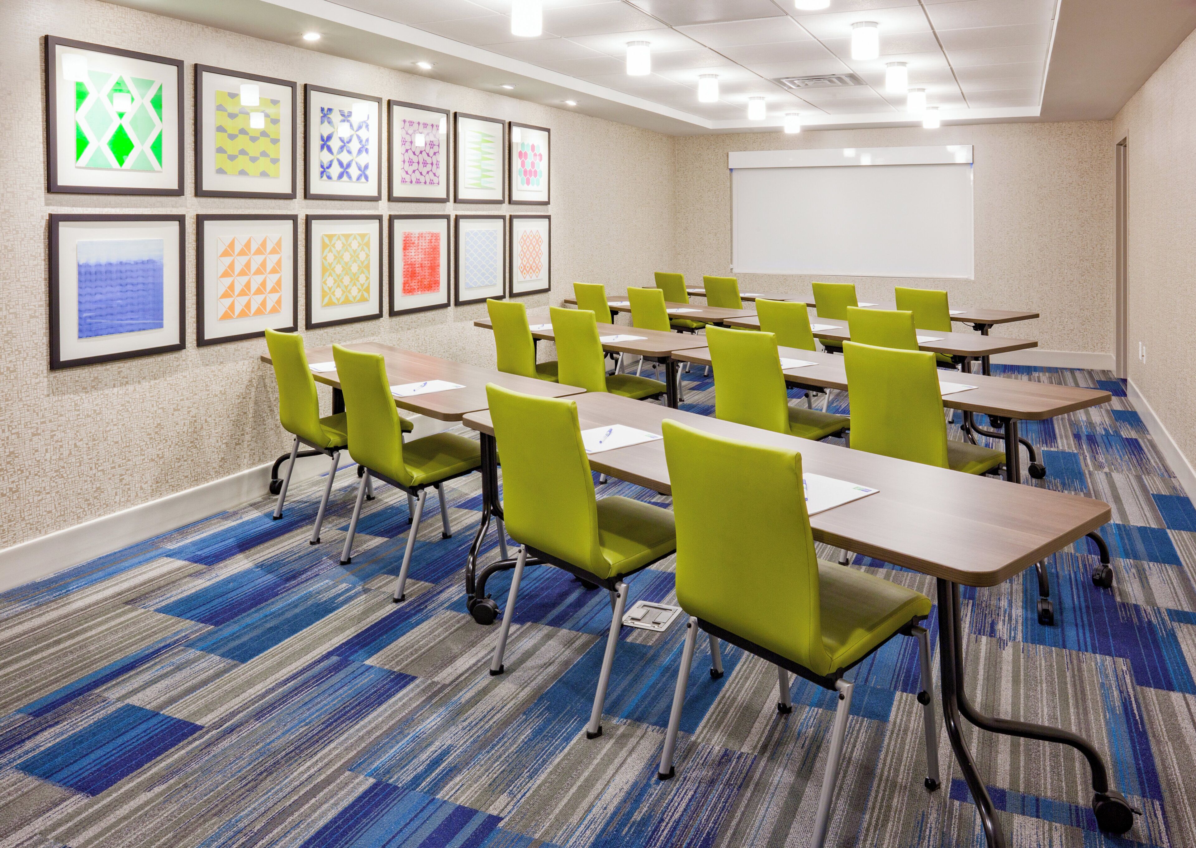 A conference room with multiple tables and chairs, a whiteboard, and framed artwork on the wall.