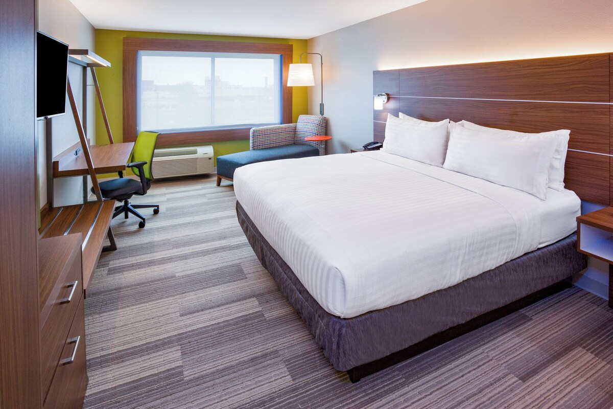 A hotel room with a large bed, a desk, a chair, a TV, and a window.
