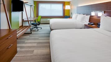 Quarto de hotel com duas camas, uma mesa com cadeira, televisão e janela com vista.