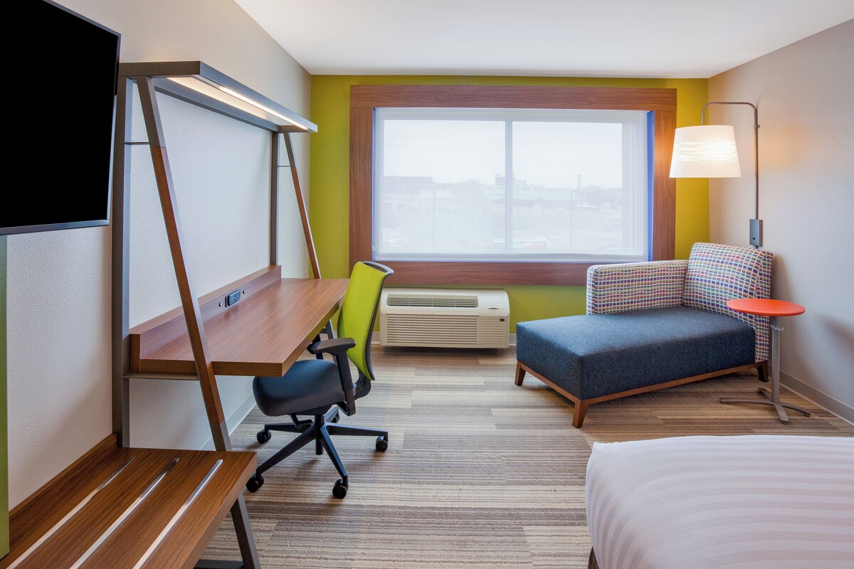 A hotel room with a desk, chair, sofa, bed, window, and lamp.