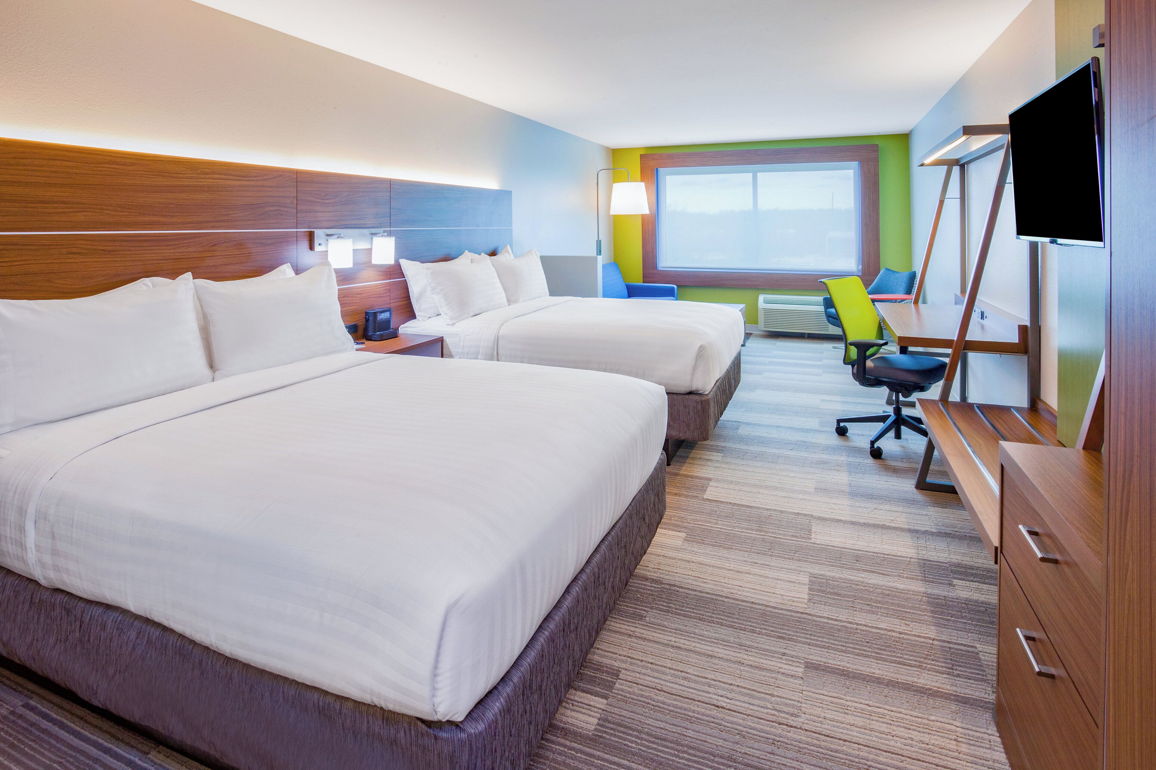 Habitación de hotel con dos camas, un escritorio, una silla, un televisor y una ventana.