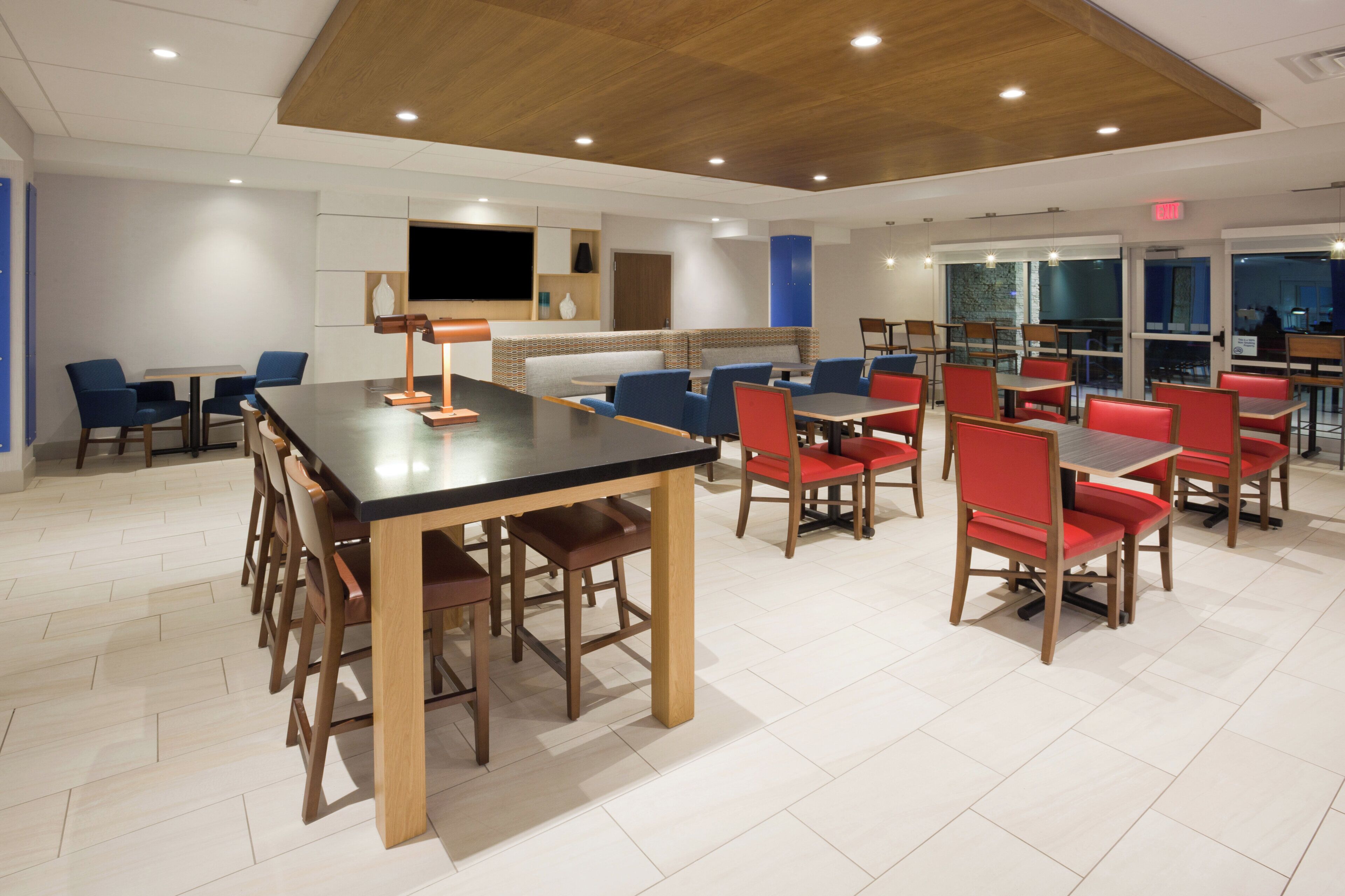 A modern dining area with wooden tables and chairs, a flat-screen TV, and a patterned wall.