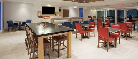 A modern dining area with wooden tables and chairs, a flat-screen TV, and a patterned wall.