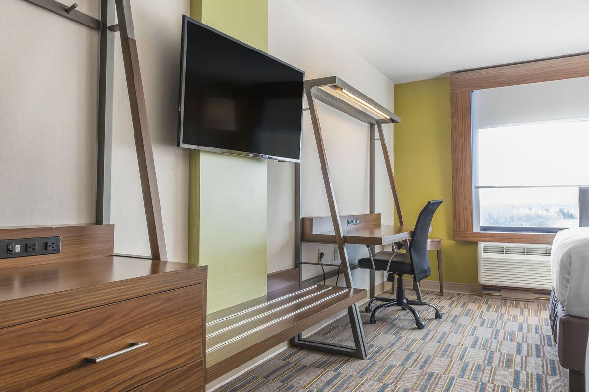 A hotel room with a desk, chair, TV, and a bed.