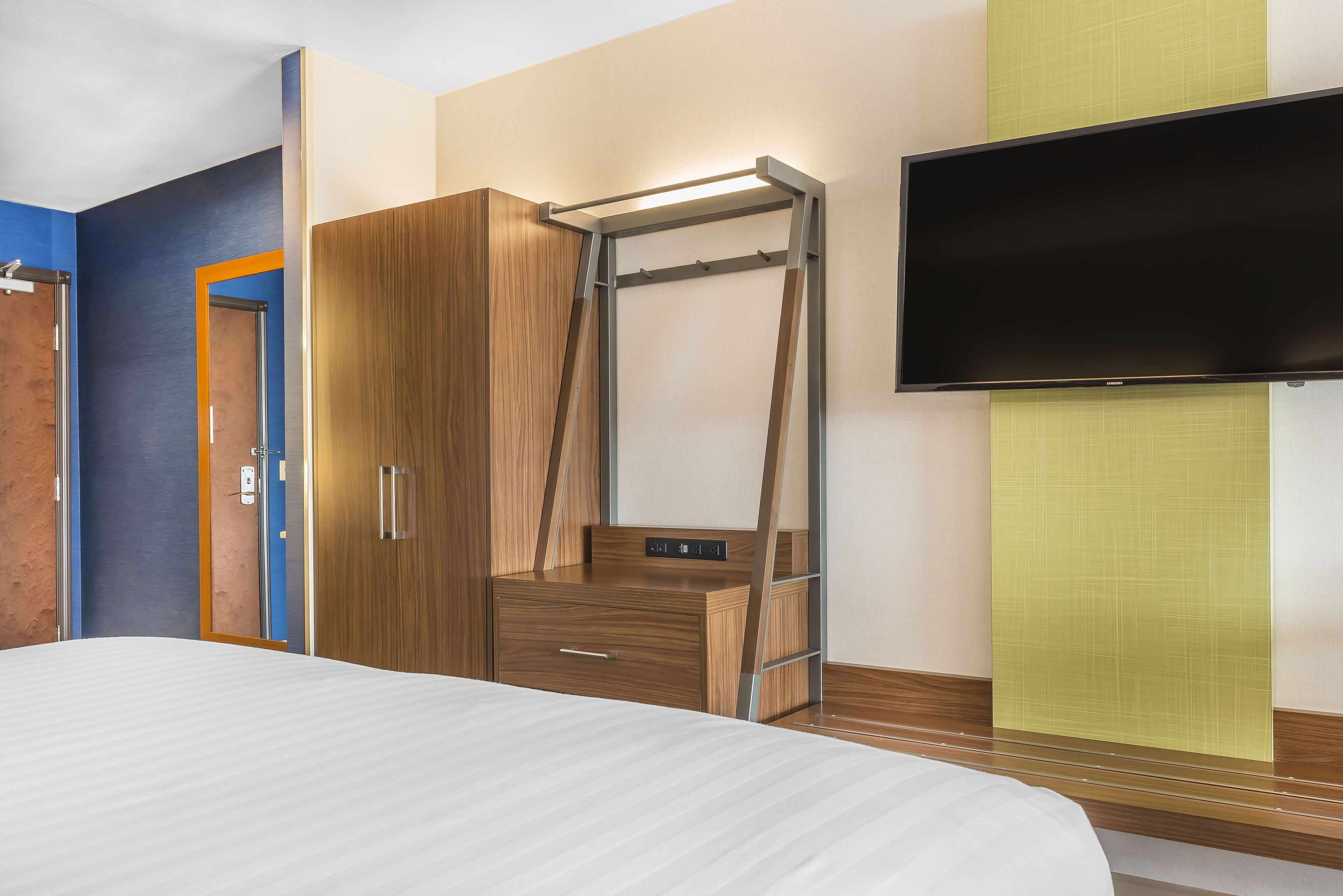 A hotel room with a bed, a wardrobe, a TV, and a wall-mounted shelf.