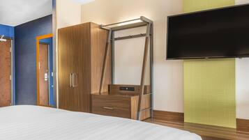 A hotel room with a bed, a wardrobe, a TV, and a wall-mounted shelf.