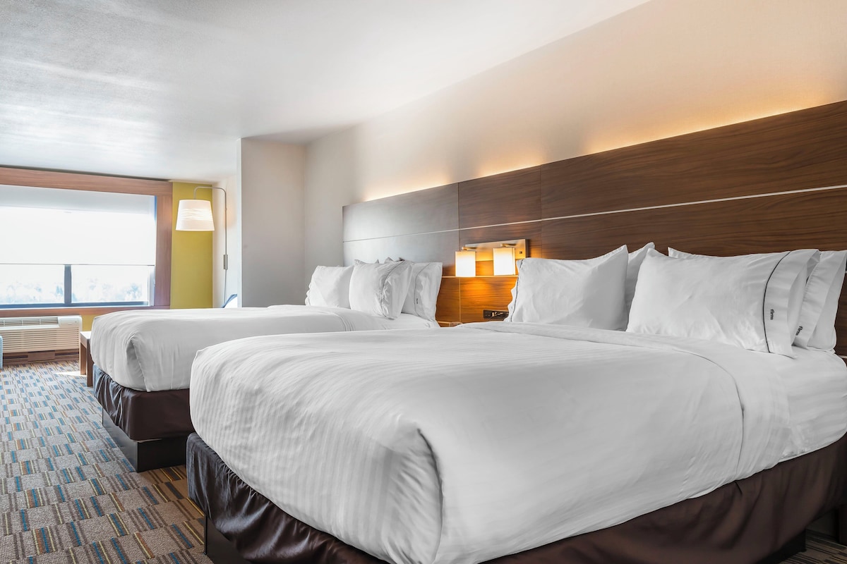 A hotel room with two beds, a large window, and a view of the city.