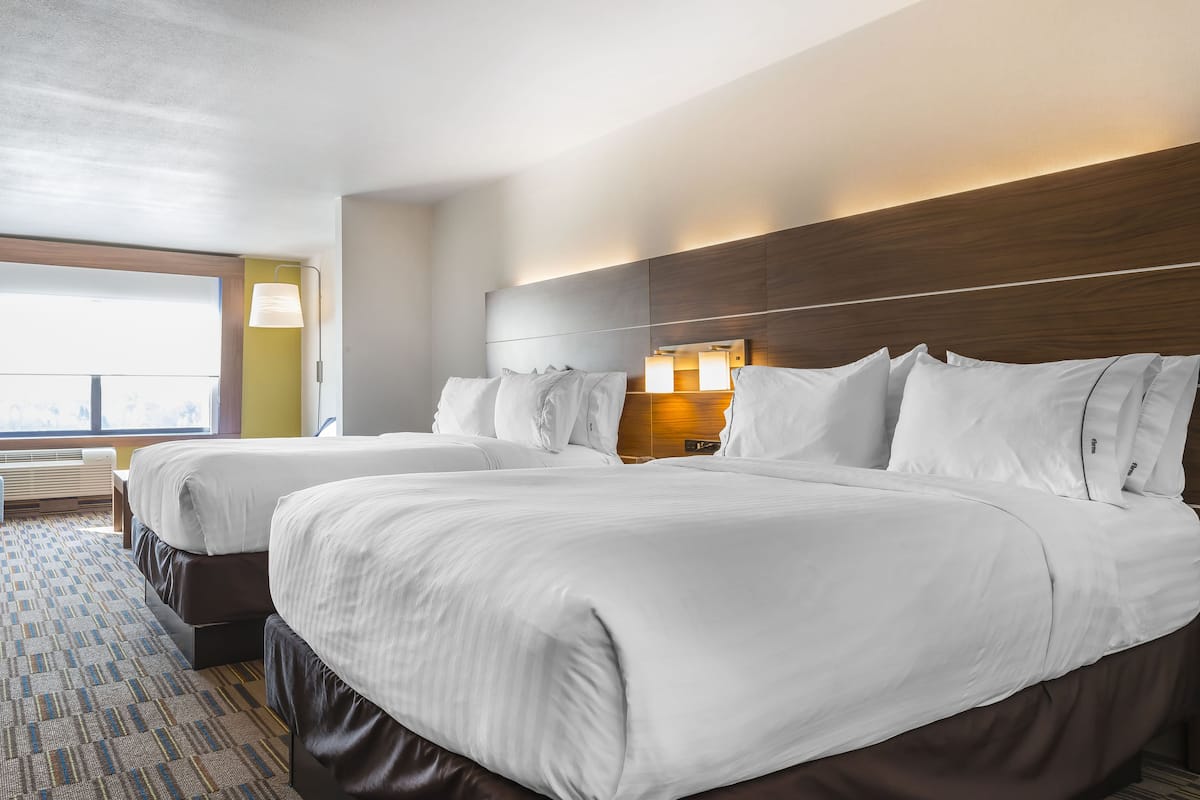 A hotel room with two beds, a large window, and a view of the city.