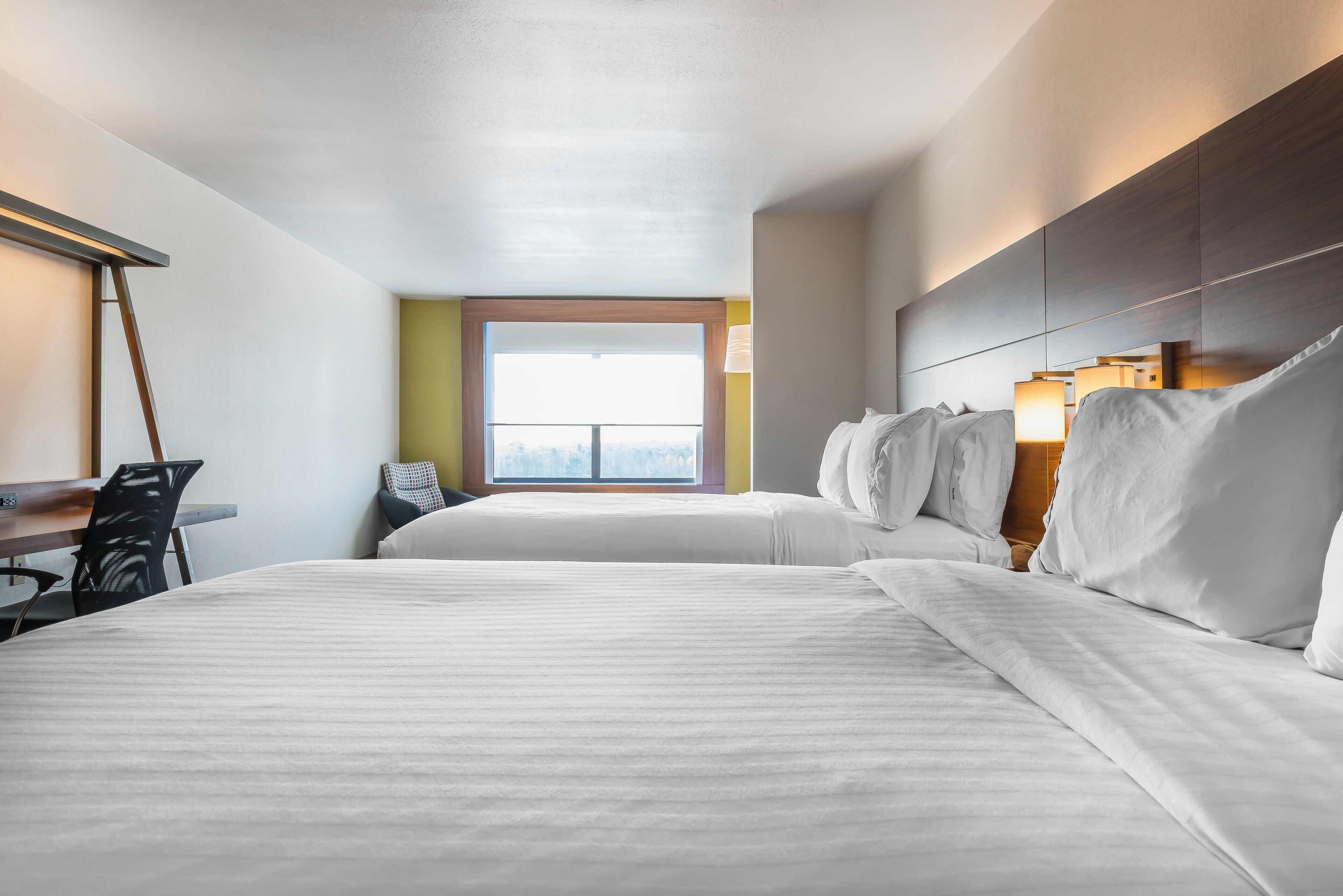 Habitació d'hotel amb dos llits, un escriptori, una cadira i una finestra amb vistes.