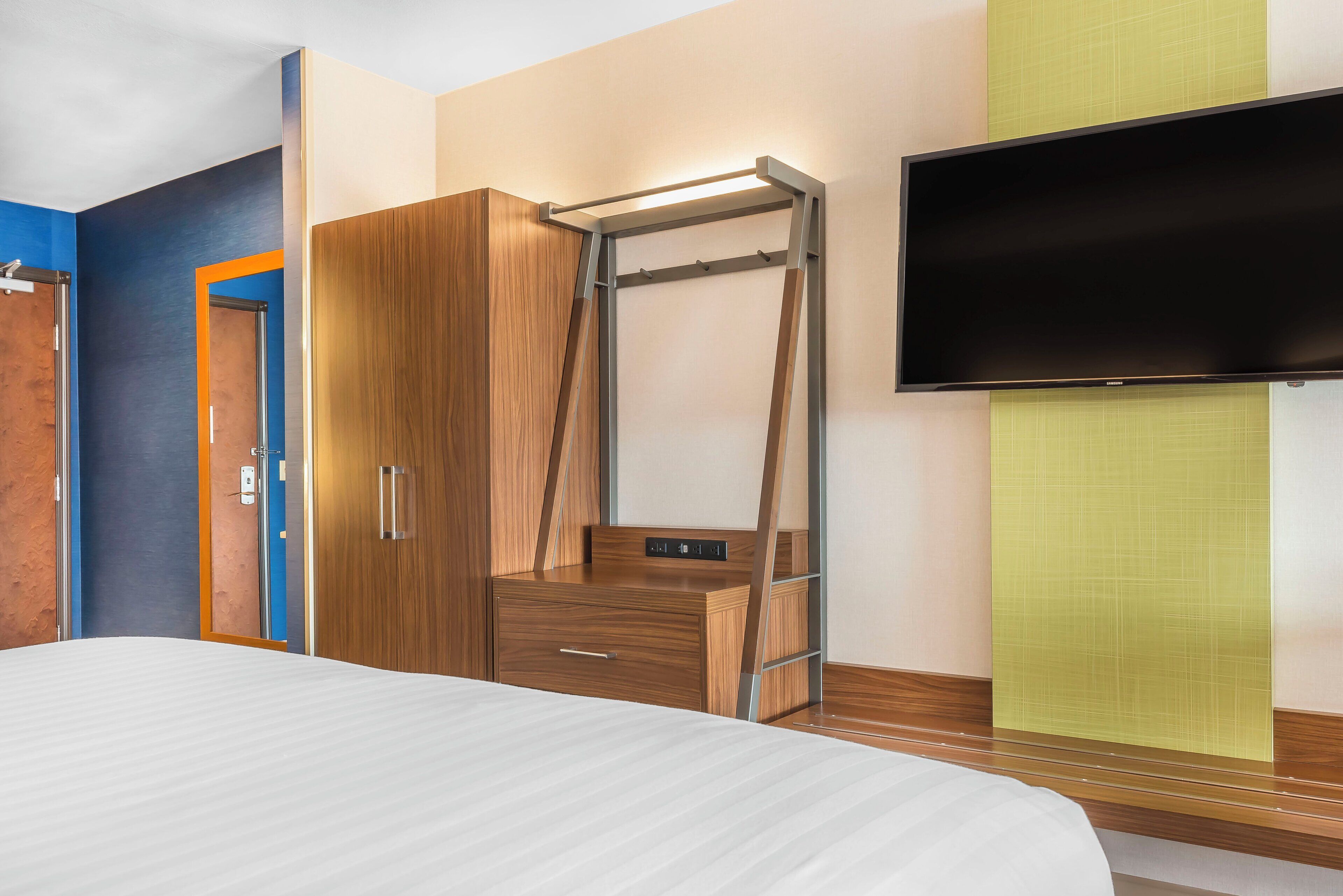 A hotel room with a bed, a wardrobe, a television, and a wall-mounted shelf.