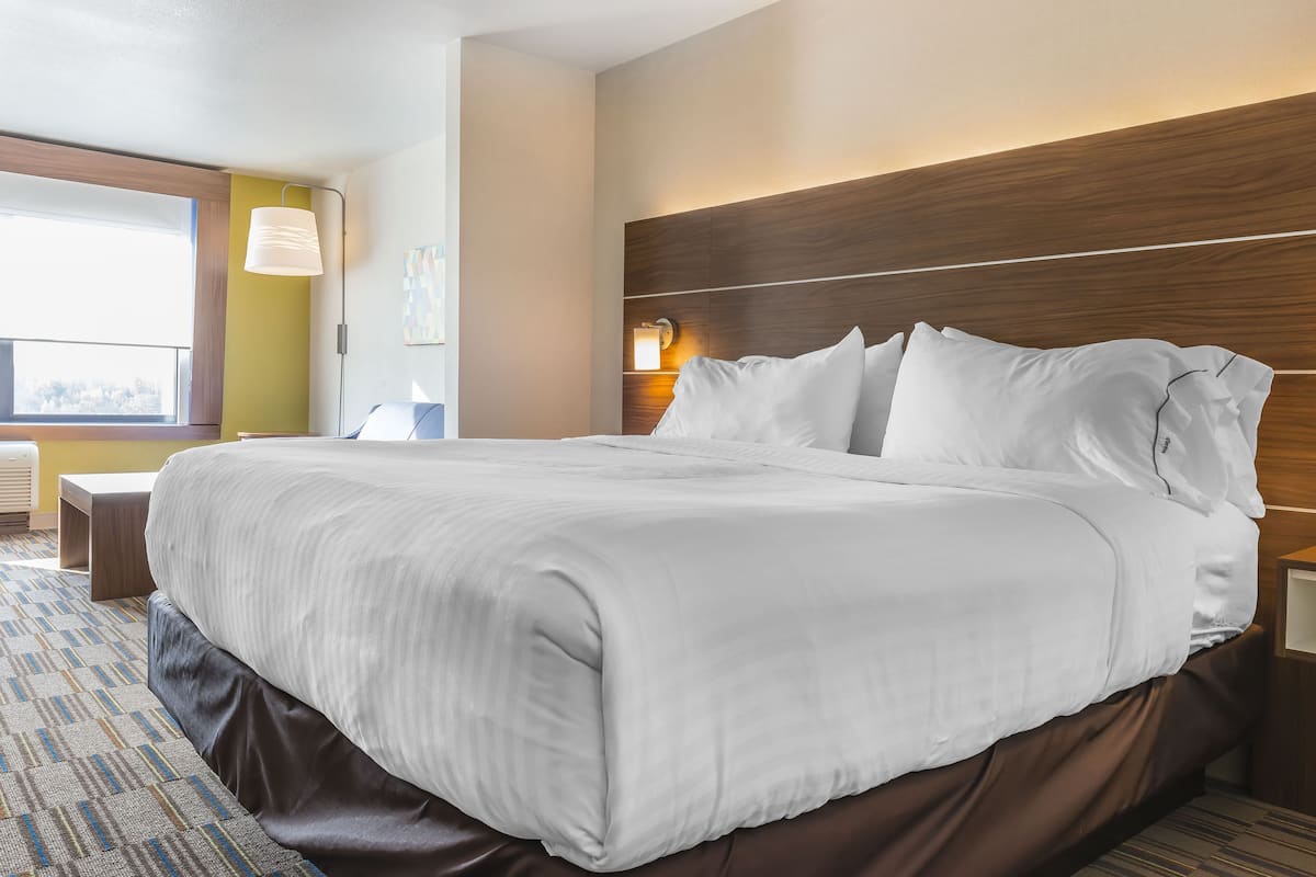A large bed with white linens, a wooden headboard, and a bedside table with a lamp.