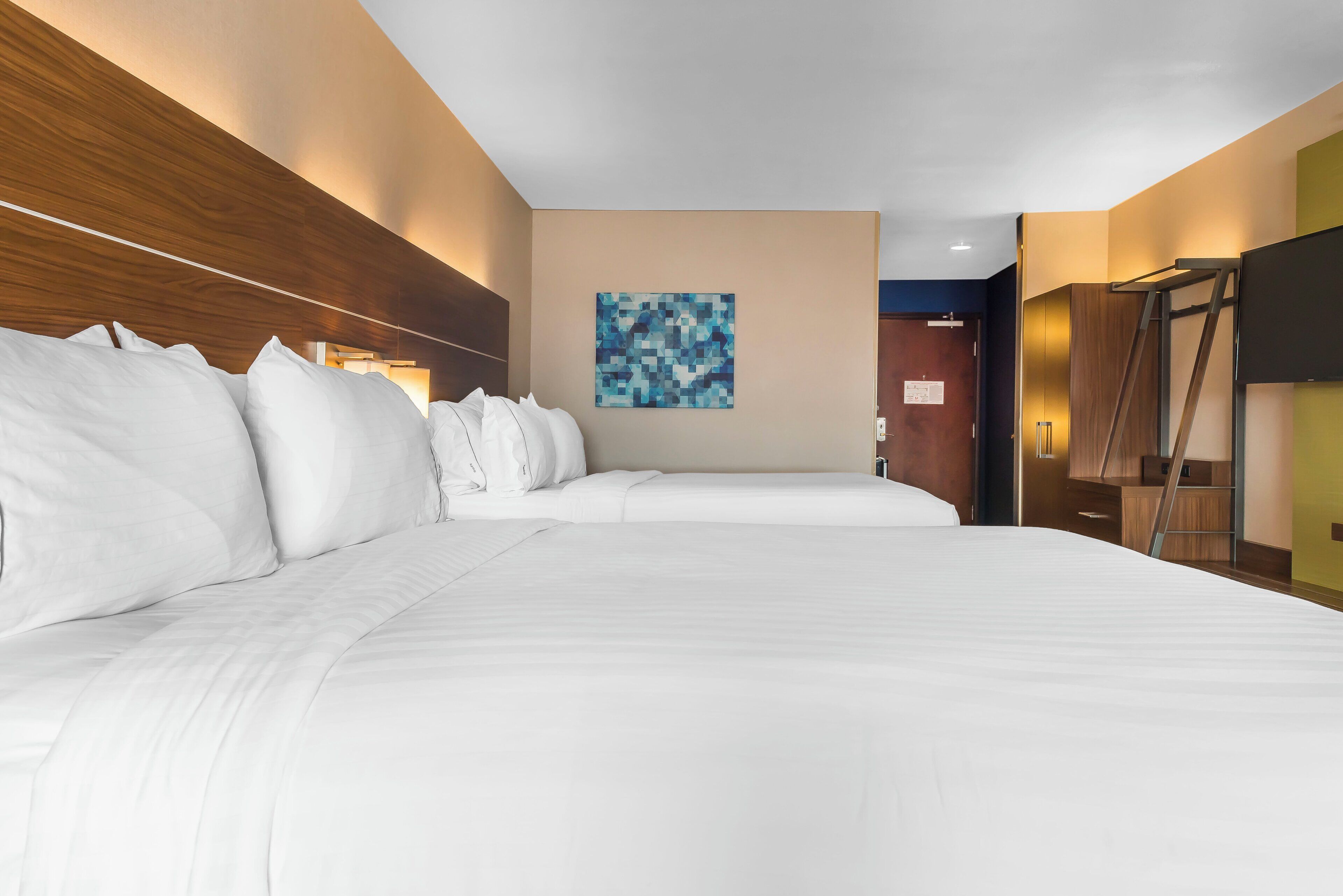 A hotel room with a large bed, a headboard, a wall-mounted artwork, and a television.