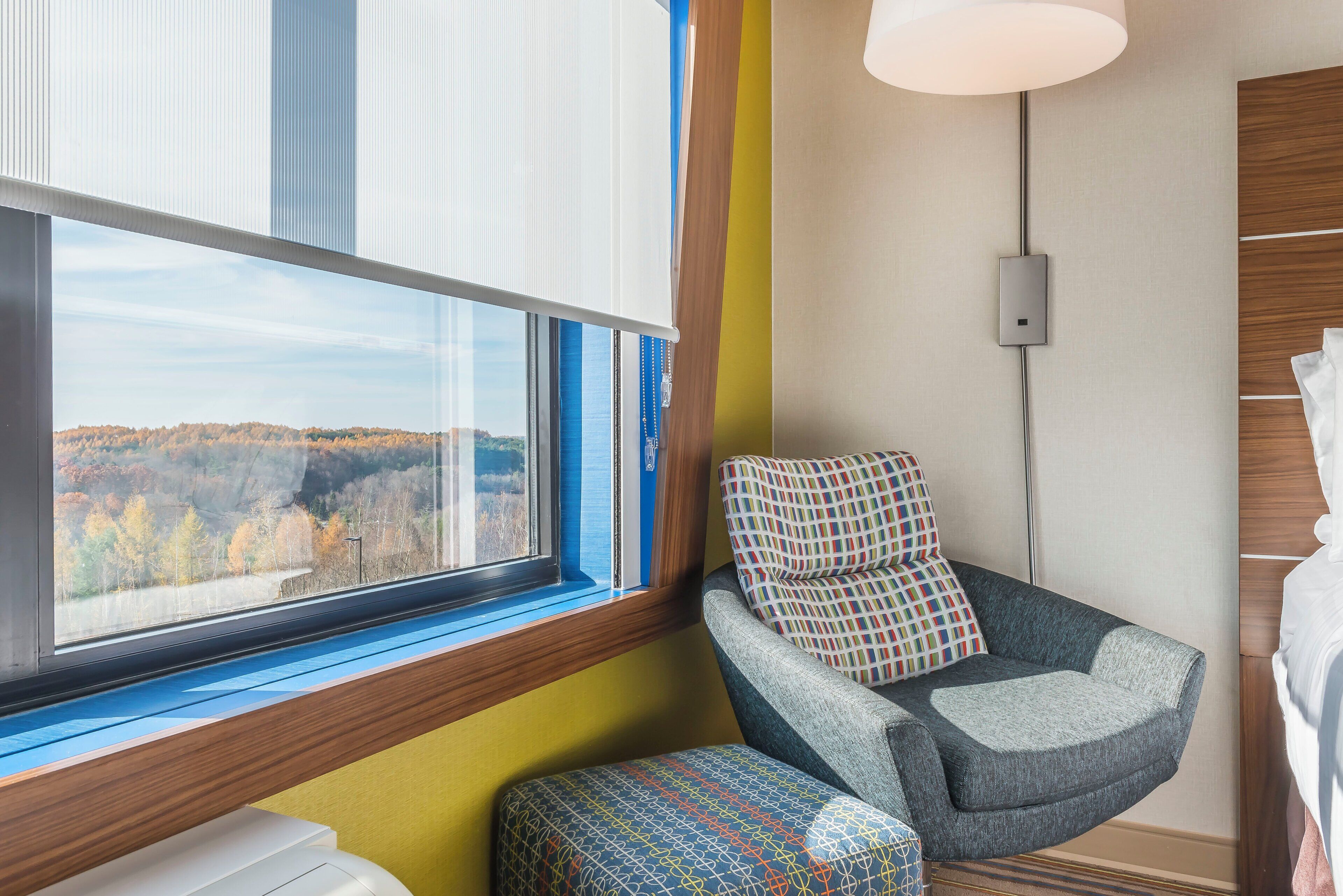 Une chambre moderne avec une grande fenêtre, un fauteuil à motifs et un petit pouf.