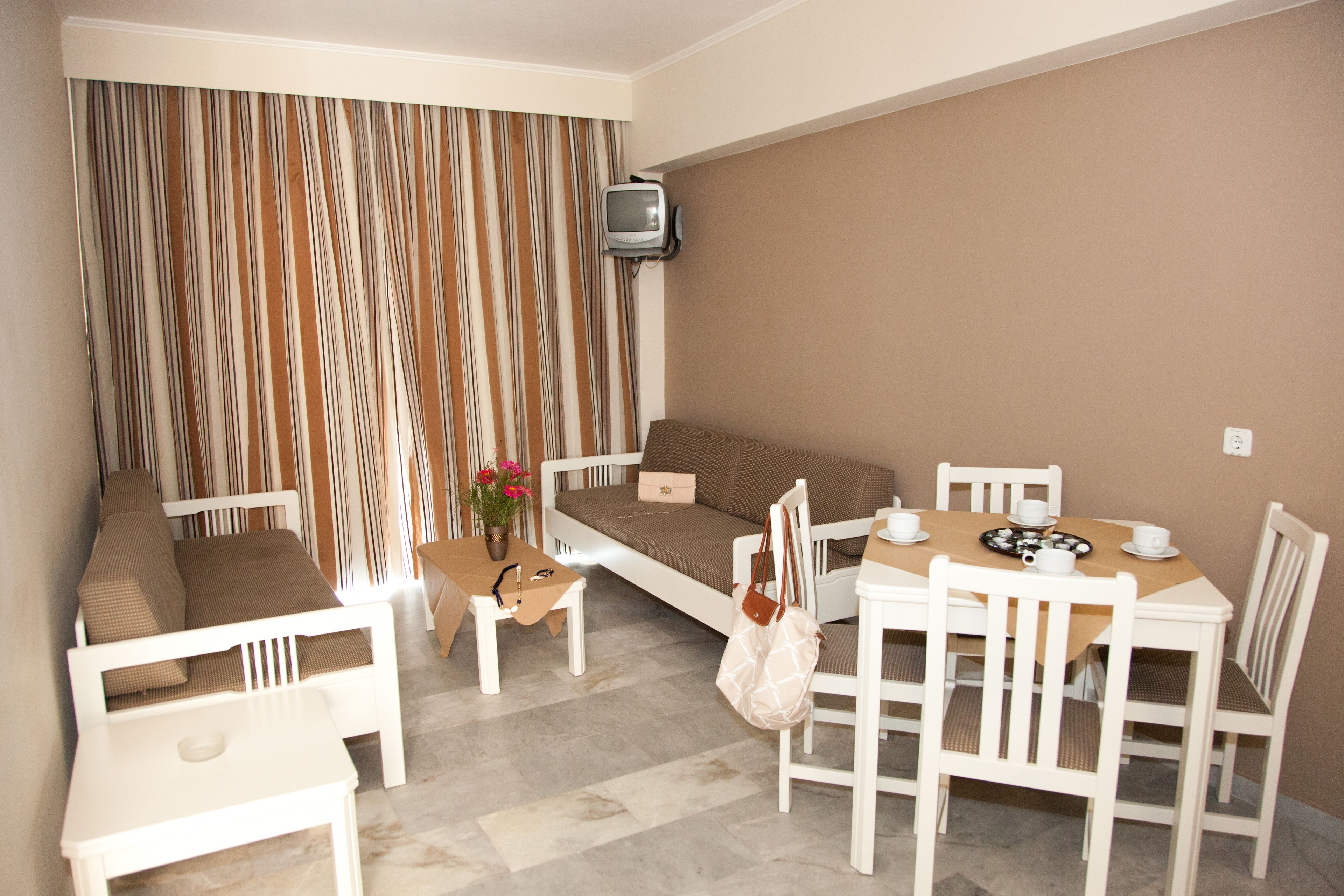 A room with a sofa, dining table, chairs, a small TV, and a curtain with a striped pattern.