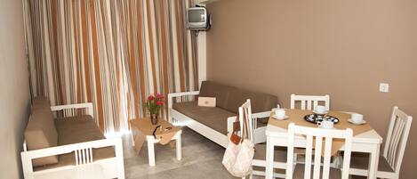 A room with a sofa, dining table, chairs, a small TV, and a curtain with a striped pattern.