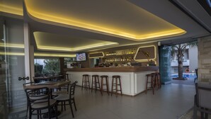 A modern bar area with a central island, bar stools, and a seating arrangement. - Golden Bay Suites (Chania)