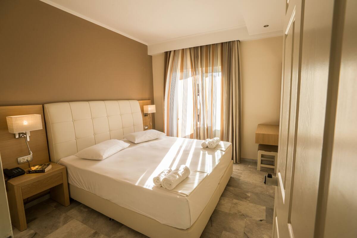 A hotel room with a large bed, bedside tables, a nightstand, and a window with curtains.