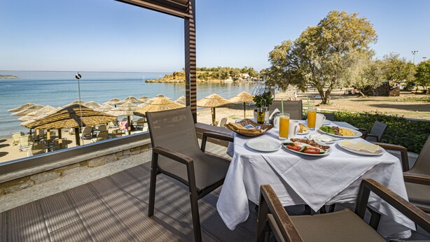 A seaside dining area with a table set for two, overlooking the ocean. - Golden Bay Suites (Chania)