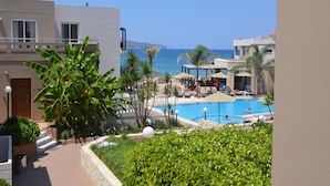 A resort with a swimming pool, palm trees, and a view of the sea. - Golden Bay Suites (Chania)