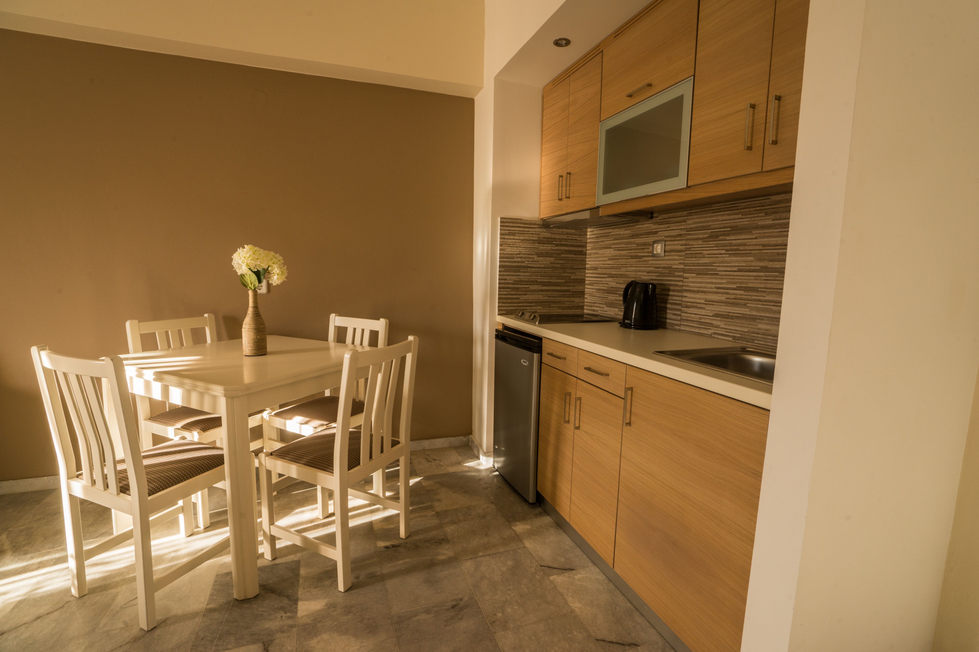 A modern kitchen with wooden cabinets, a stainless steel sink, and a dining area with a white table and chairs.