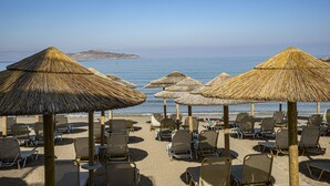 A beach with rows of sun loungers and thatched umbrellas, a clear sky, and calm sea. - Golden Bay Suites (Chania)