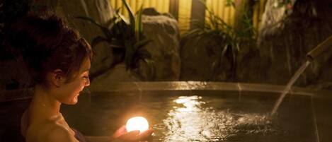 A person holding a glowing object in a water feature with rocks and plants in the background.