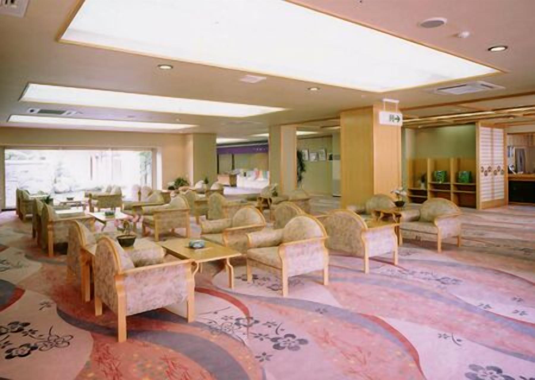 Un amplio vestíbulo de hotel con varias zonas de estar, un mostrador de recepción y vistas al exterior.