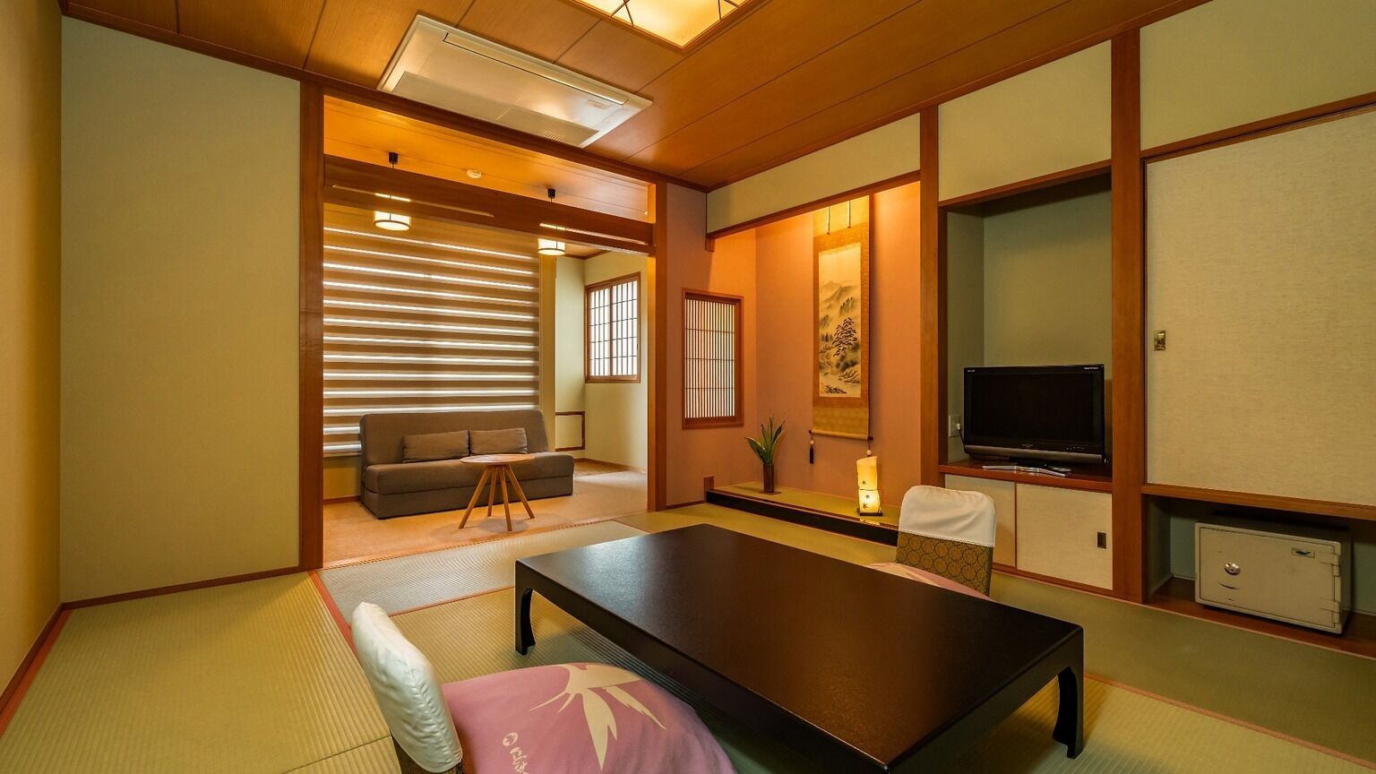 A traditional Japanese room with tatami flooring, a low table, a sofa, a television, and sliding doors.