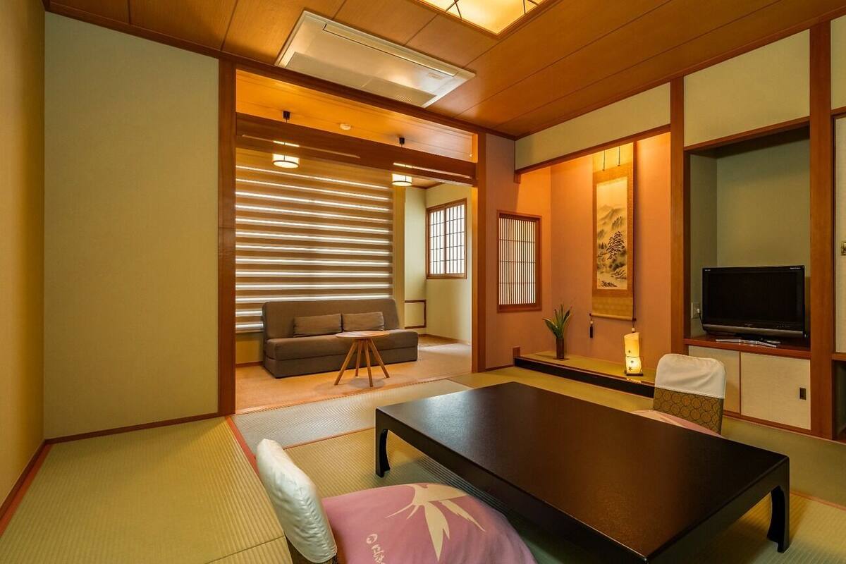Une pièce de style japonais traditionnel, avec un sol recouvert de tatamis, une table basse, un canapé, un téléviseur et des portes coulissantes.