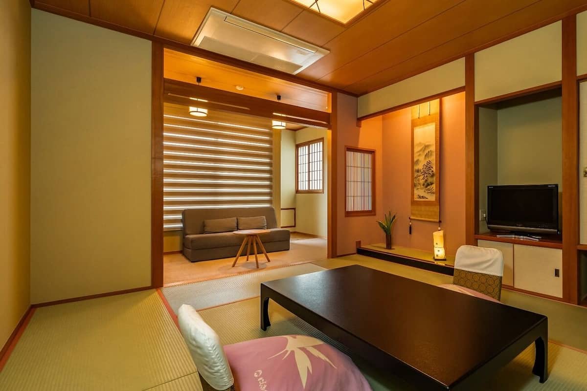A traditional Japanese room with tatami flooring, a low table, a sofa, a television, and sliding doors.