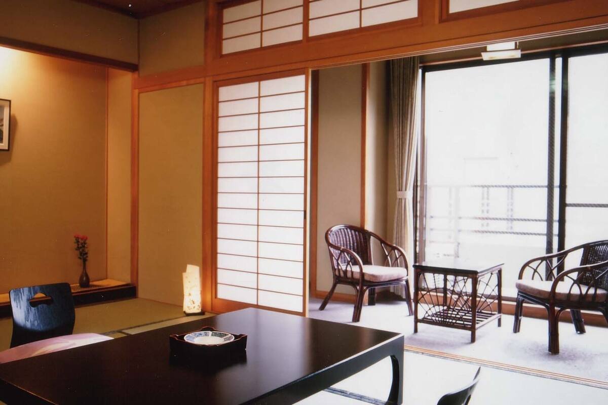 Une pièce de style japonais traditionnel, avec un sol recouvert de tatamis, une petite table sur laquelle est disposé un service à thé, une chaise et une porte coulissante donnant sur un balcon.