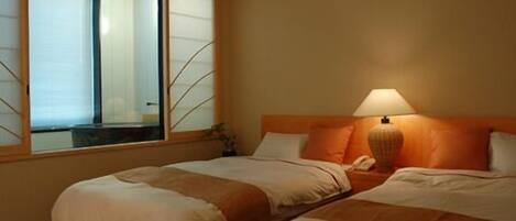 A hotel room with two beds, a window with blinds, a bedside lamp, and a wooden headboard.