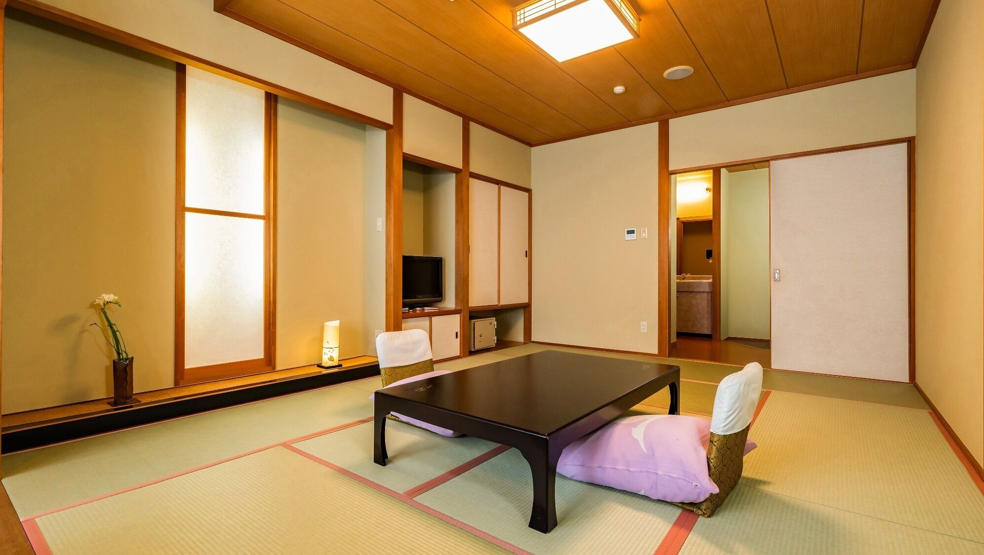 A traditional Japanese room with tatami flooring, a low table, a television, and sliding doors.