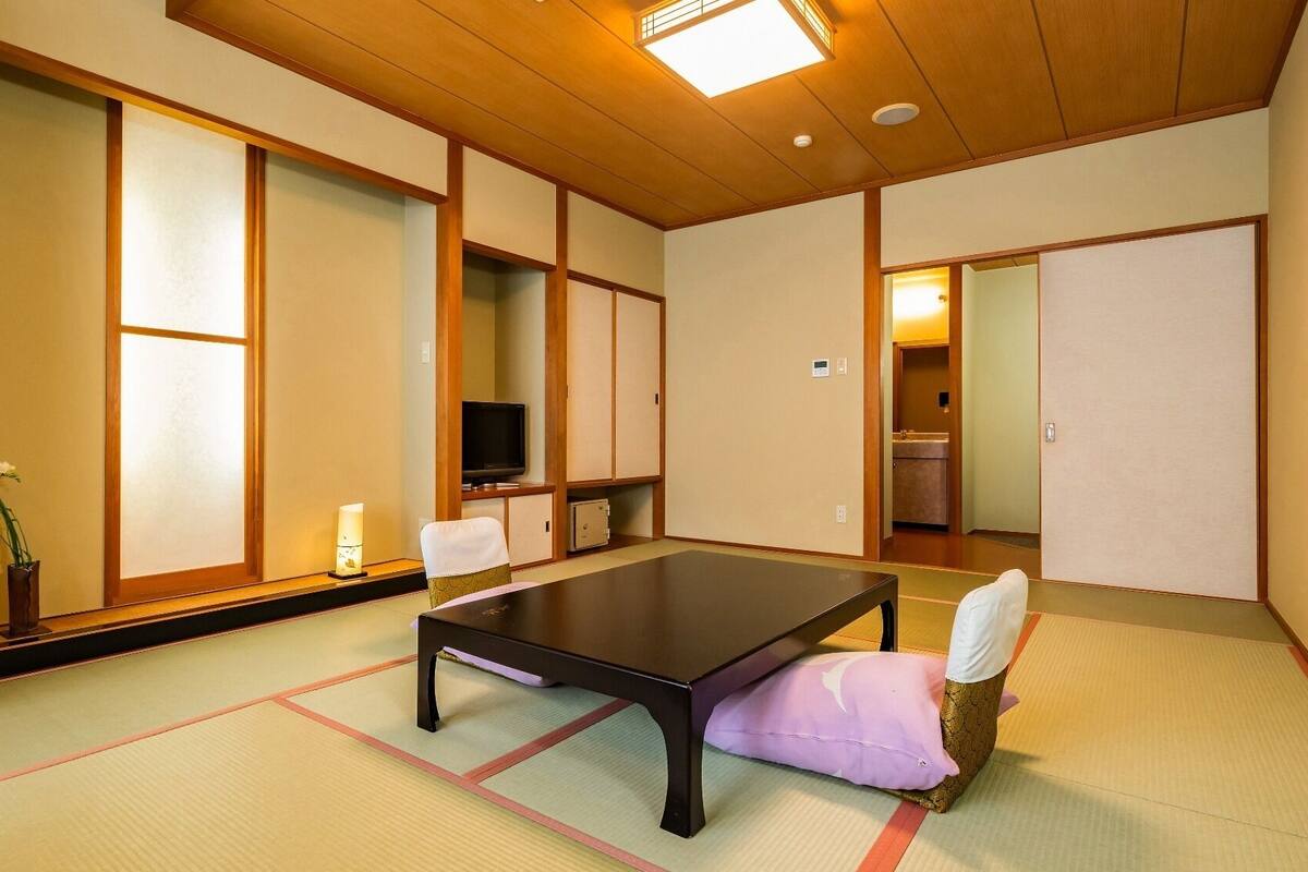Une pièce de style japonais traditionnel, avec un sol recouvert de tatamis, une table basse, un téléviseur et des portes coulissantes.