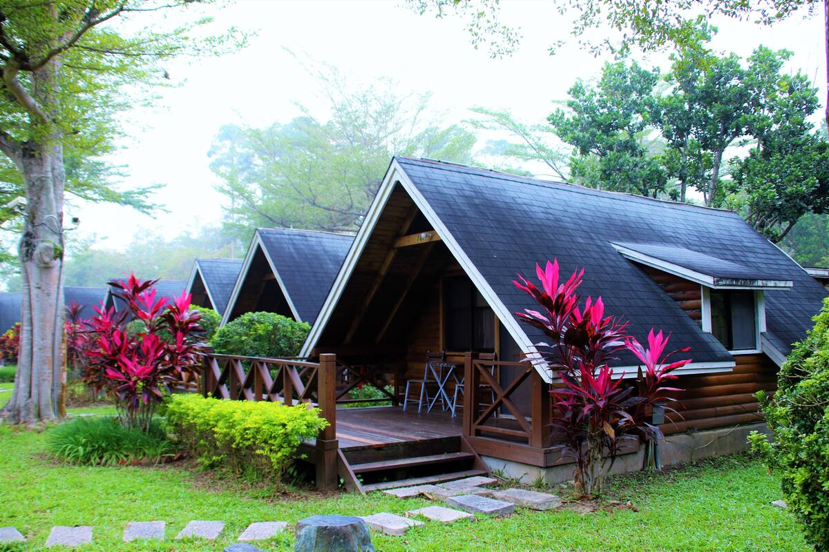 A row of log cabins with a wooden deck and steps leading up to the entrance.